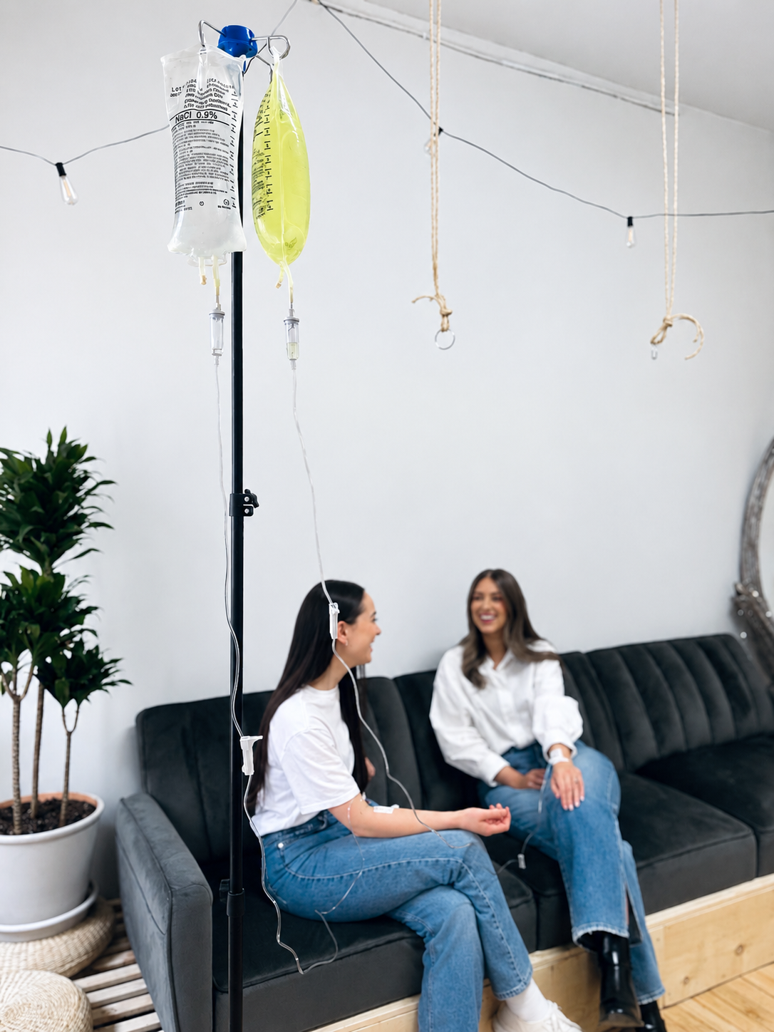 Friends chatting on a velvet couch beside an IV pole in the Northbound Wellness clinic